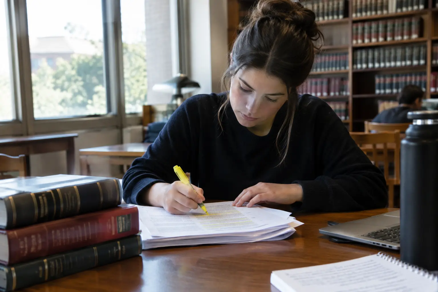 Estudante de direito a sublinhar um acórdão impresso numa biblioteca
